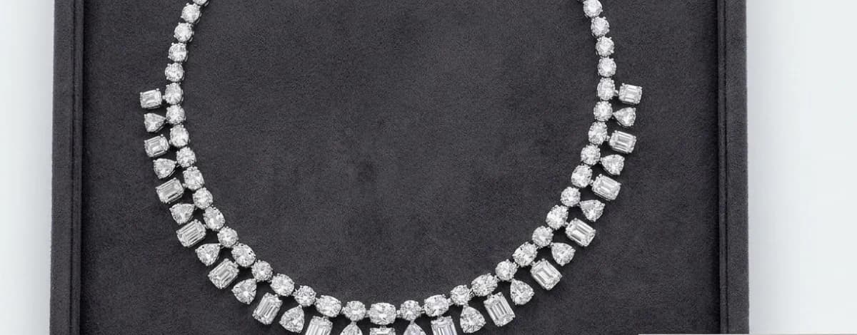 A diamond necklace of alternating pear, emerald and round stones laid out in a grey suede case.