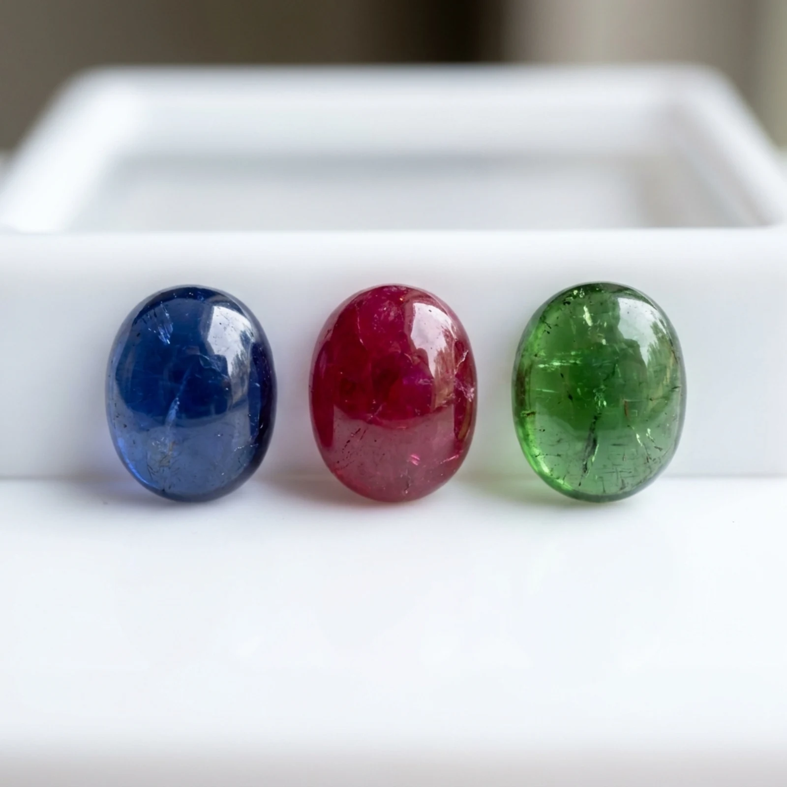Three cabochon stones — a blue sapphire, a red ruby and a green tourmaline — stood in a row on a white tray.
