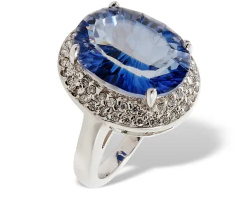 A white metal ring set with a large oval stone inside a border of small brilliants.