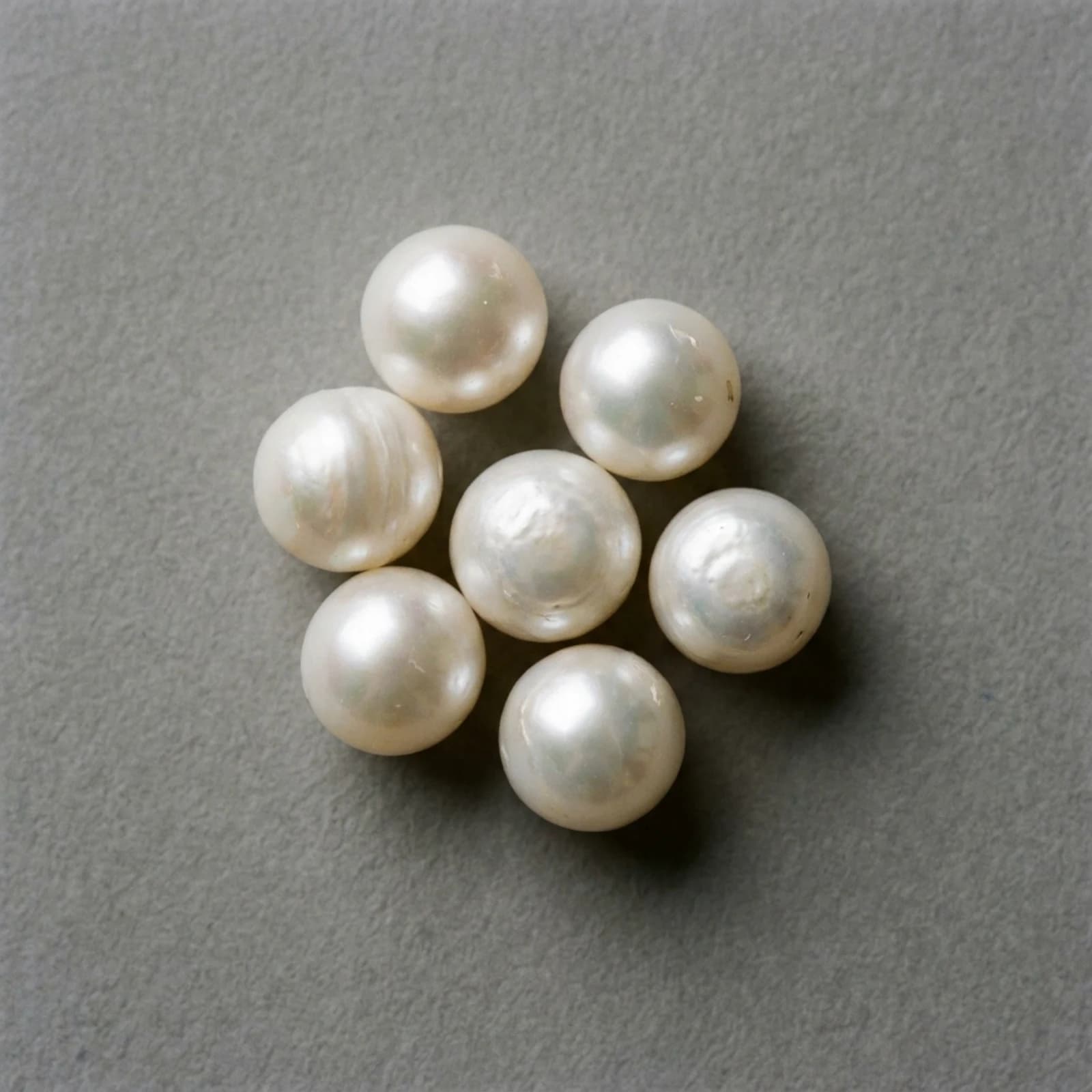 Seven loose white pearls grouped closely together on a neutral grey ground, seen from above.