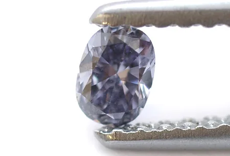 An oval brilliant diamond held in a pair of tweezers.